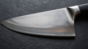 Carbon steel knife with oil, resting on a dark surface.