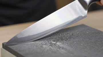 Chef's knife being sharpened on a whetstone.