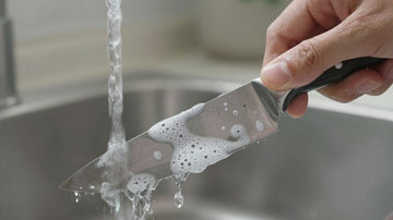 Hand washing a clean kitchen knife under running water.